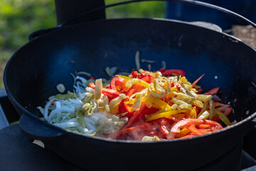 The process of cooking lagman in a cauldron on an open fire. Cooking a traditional dish of Middle East cuisine with homemade noodles, beef and vegetables. Outdoor cooking concept.