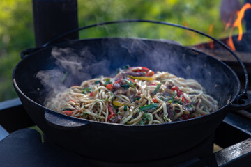 The process of cooking lagman in a cauldron on an open fire. Cooking a traditional dish of Middle East cuisine with homemade noodles, beef and vegetables. Outdoor cooking concept.
