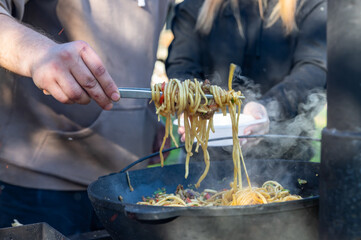 A man hand holding a fork with homemade noodles. Lagman. Taditional dish of Middle East cuisine with noodles, beef and vegetables. Outdoor party or picnic.