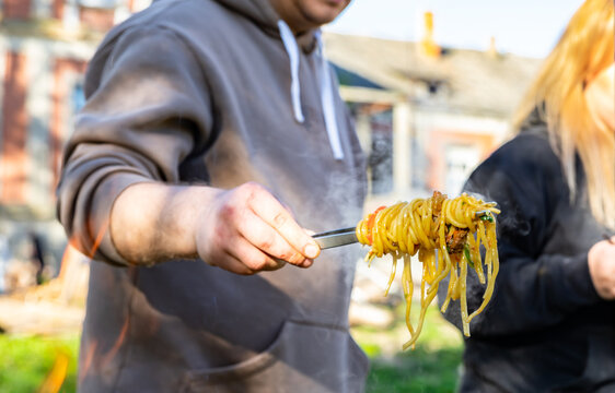 A man hand holding fork with homemade noodles. Lagman. Taditional dish of Middle East cuisine with noodles, beef and vegetables. Outdoor party or picnic.