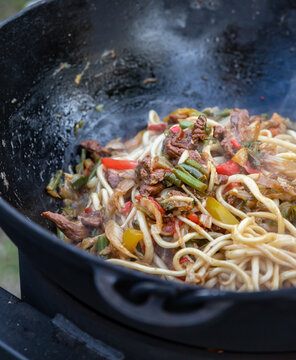 The process of cooking lagman in a cauldron on an open fire. Cooking a traditional dish of Middle East cuisine with homemade noodles, beef and vegetables. Outdoor cooking concept.