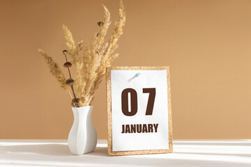 january 7. 7th day of month, calendar date.White vase with dried flowers on desktop in rays of...