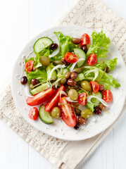 Healthy salad with various tomatoes, cucumber, olives and capers. White wooden background. Top view.	