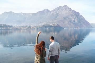 Soft focus, back view couple enjoying romantic date on shores of Lake Lecco, Italy. People in love on background of mountains, water outdoors. Romantic relationships, Adventures, holidays. Copy space