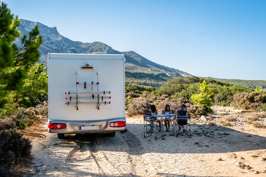 Family traveling with motorhome are eating breakfast on a beach.
