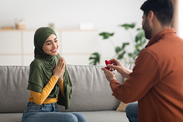 Happy Muslim Man Proposing To Woman Offering Engagement Ring Indoors