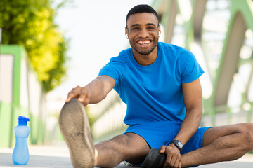 Happy millennial black-bearded sportsman doing leg exercises while stretching on the floor