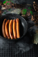 Fried sausages in a frying pan on a background of stones and moss with smoke