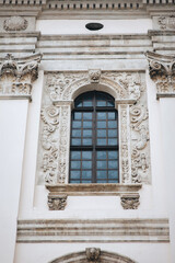 Antique openwork baroque window with a lattice frame and decorative stucco on a light cream wall. Jesuit Church in Lviv.