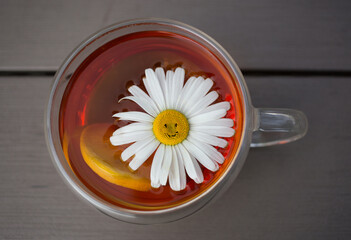 Good morning. The concept of a happy day with a cup of morning fragrant tea. cup of tea with lemon and large flower of chamomile with a smile. Rest and tea drinking. View from above
