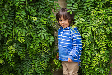Portrait of a little handsome baby boy playing outdoor in the park. Child hiding surraunded green leaves