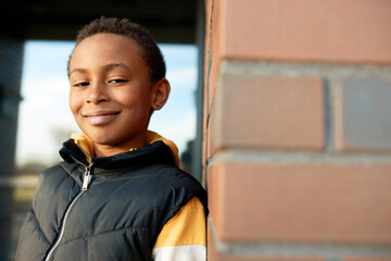 Outdoor picture of handsome confident happy boy of african ethnicity standing over red brick wall,...