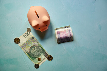 różowa świnka skarbonka, monety i banknoty na niebieskim tle  © Marcin Łazarczyk