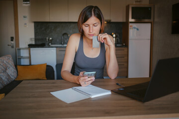 young asian woman at home, remote work at laptop. shopping online at home, lady is holding credit card and using smartphone and computer.