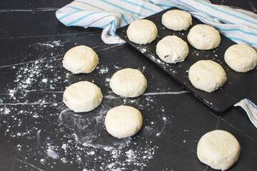 Board with uncooked cottage cheese pancakes and ingredients on black background