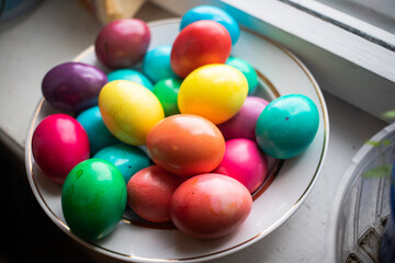 painted multi-colored chicken eggs in a wide white plate as a symbol of the holiday of Catholic...