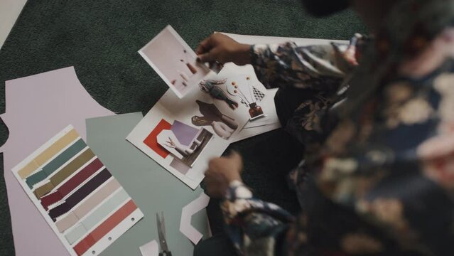 Top view of male fashion designer making mood board from different aesthetic pictures sitting on floor in workshop