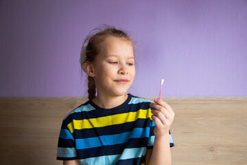 a child girl in a striped turtleneck demonstrates a cotton swab for ears as a symbol of purity