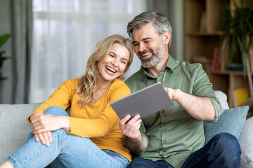 Cheerful Middle Aged Couple Relaxing With Digital Tablet At Home