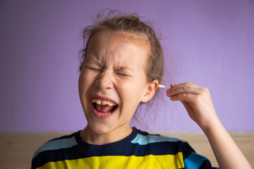girl child in a striped turtleneck shows pain due to a cotton stick in the ear, where it is very dirty