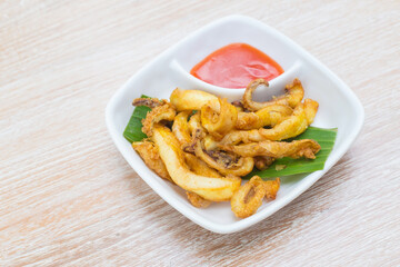 Sun dried squid was served with chili sauce. It's a delicious Thai food on the wooden table.