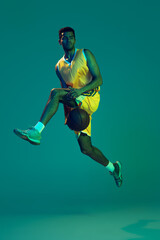 Fototapeta na wymiar Portrait of young man, professional backetball player in motion, training isolated over blue background in neon light
