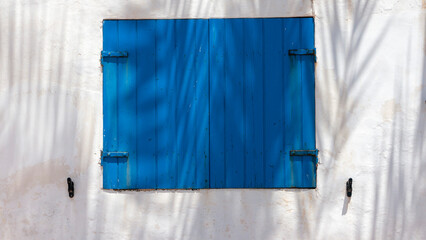 Ventana de madera azul intenso cerrada en pared blanca de casa de playa estilo mediterraneo