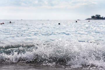 Sea waves splashing at beachs shore with boats and swimmers in background