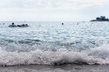Sea waves splashing at beachs shore with boats and swimmers in background