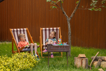 A little boy and a little girl lie on a sun lounger in the garden. Net sunny weather, two children get along and sunbathe on sunbeds.