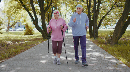 Active senior elderly couple 80 years old in summer park. Caucasian grandfather man training Nordic...