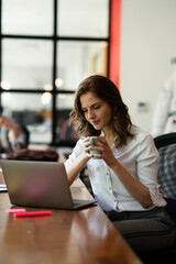 Obraz premium Happy businesswoman working on laptop. Portrait of beautiful businesswoman drinking coffee in the office