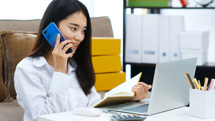 Work from home, Young asian woman talking mobile phone and holding notebook while working at home office, People and technology communication, e commerce, online business, e learning, education