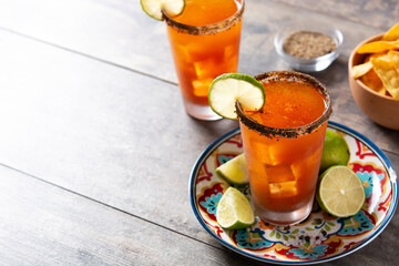Homemade michelada cocktail with beer, lime juice,hot sauce,salted rim and tomato juice on wooden table. Copy space