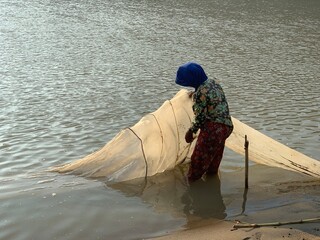 a strong Indonesian woman pulling fishing nets and crabs from the river in the morning