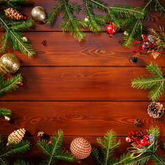 Fototapeta na wymiar Square Christmas frame with real wooden green pine tree, colorful baubles, knots with berries and other seasonal things on a wooden background. View from above.