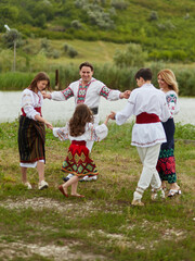 Full length image of a family with kids in traditional romanian dress in a countryside, park. Dancing outside.