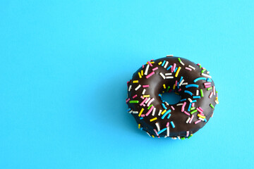 glazed chocolate doughnut with blue, pink, yellow and green sprinkles isolated on blue background