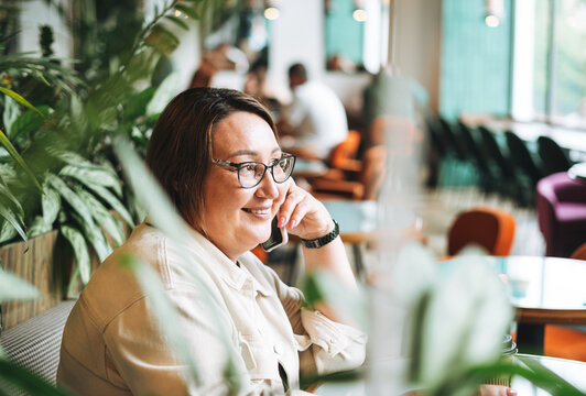 Adult brunette middle aged woman plus size body positive in casual clothes with paper cup of coffee using mobile phone in cafe
