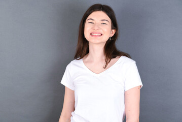 Fototapeta premium young beautiful Caucasian woman wearing white T-shirt over studio grey wall with broad smile, shows white teeth, feeling confident rejoices having day off.