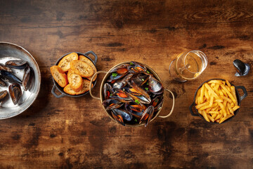 Cooked mussels with French fries and toasted bread, with a glass of white wine, top shot on a rustic wooden table with copy space