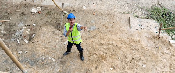 Young asian man in hardhat and  safety vest pointing at scaffolding made of wood structure while...
