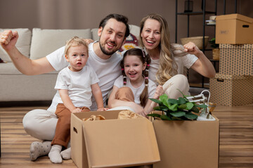 A cheerful family unpacks cardboard boxes after a move. The little girl and her brother take out the packed vases of pictures. Playing together while cleaning up.