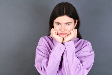 Portrait of sad young beautiful Caucasian woman wearing pink shirt over studio grey wall hands face