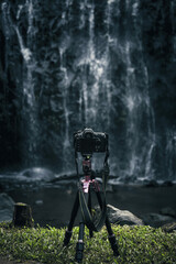 Modern camera is set on tripod for landscape photography in front of waterfall. 