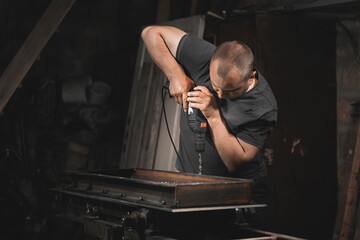 A man drills metal with a hand drill in his home workshop. Making a metal product with your own hands