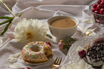 Breakfast in bed with various delicious glazed donuts on the plate, cup of coffee and sweet cherry berries. Side view.