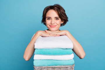 Portrait of young adorable newly wed wife doing home chores relaxing on pile of towels isolated on blue color background