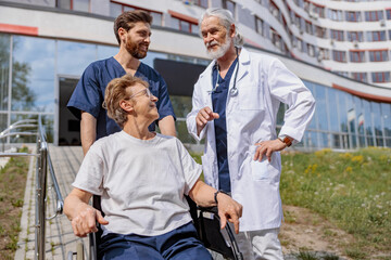 Fototapeta na wymiar Nurse and doctor talking to patient on wheelchair in hospital yard . Rehabilitation concept.