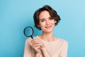 Photo of cute smart young lady working as detective find clues with magnifier glass isolated on blue color background